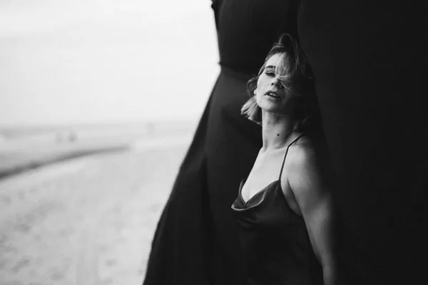 Schwarz-weiß Portrait einer Frau am Strand hinter dunklem Stoff.