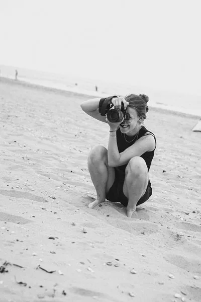 Schwarz-weiß-Portrait einer Frau, die am Strand eine Kamera hält.