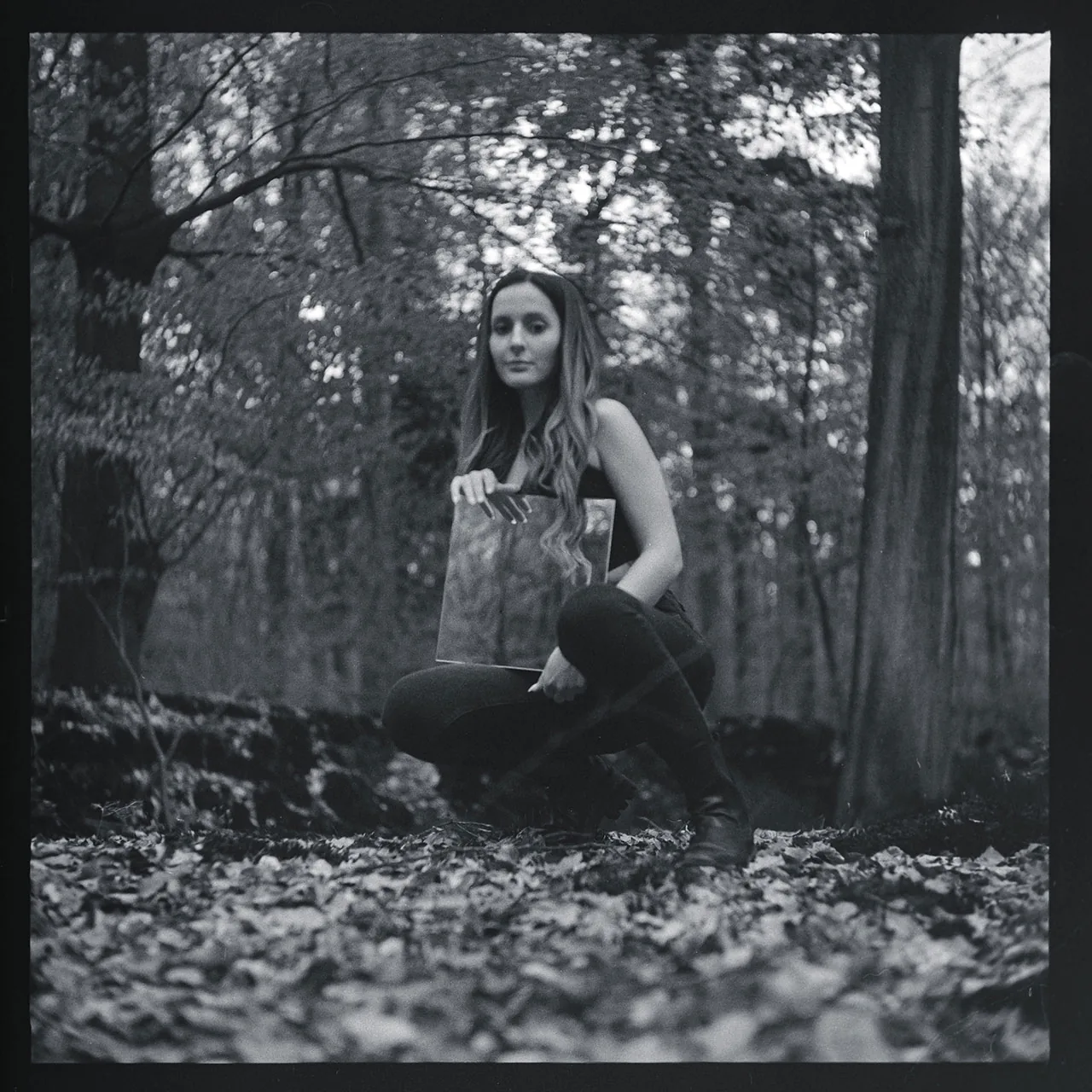 Schwarz-weiß-Portrait einer Frau, die in einem Wald ein Bild hält.