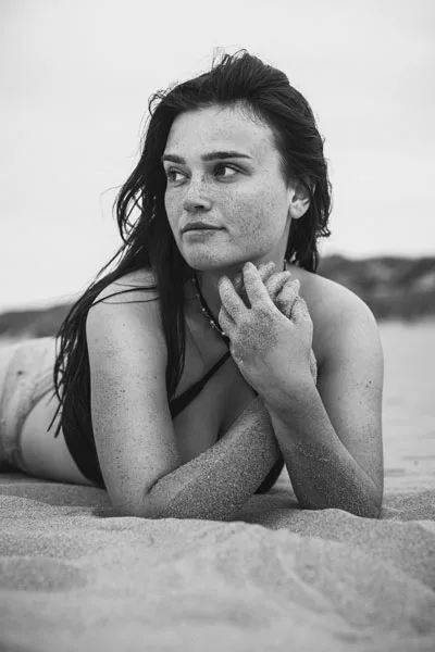 Schwarz-weiß Portrait einer jungen Frau mit Sommersprossen im Sand.