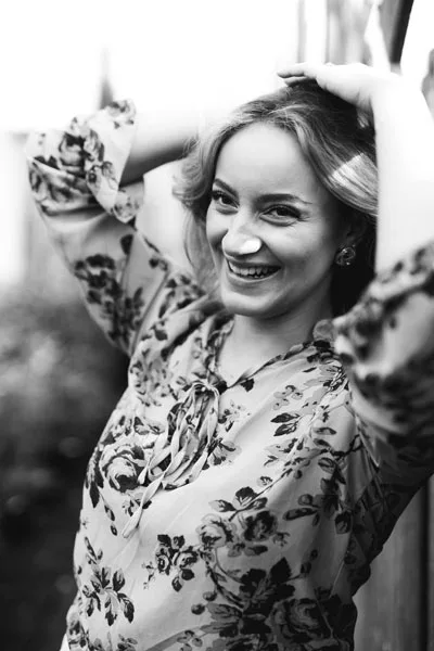 Schwarz-weiß-Portrait einer lächelnden Frau in floraler Bluse.