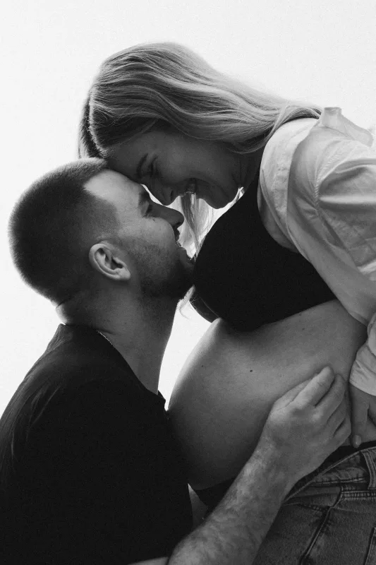 Schwarz-weiß Portrait eines Paares, bei dem die Hand des Mannes sanft auf dem Babybauch ruht.