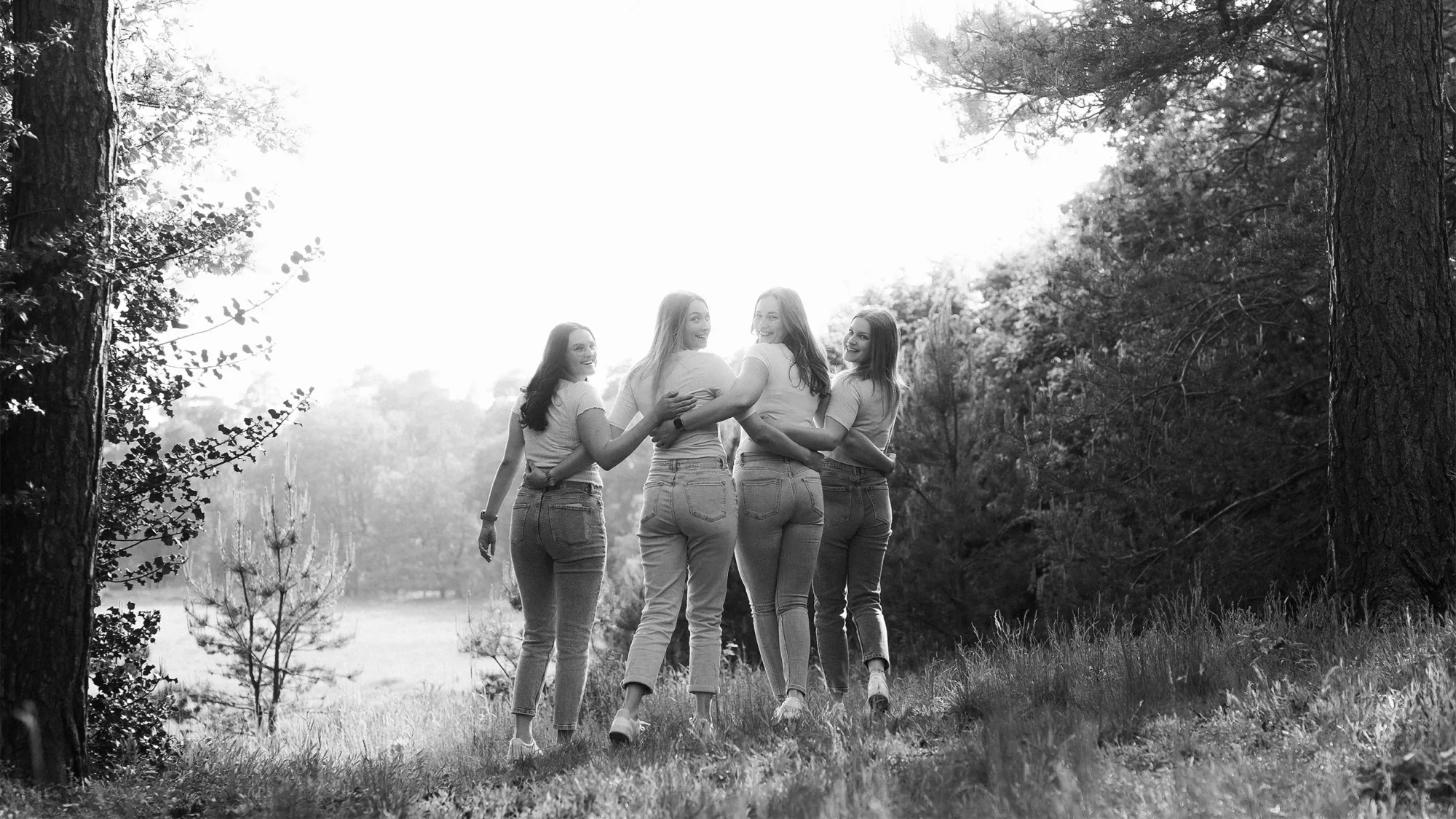Schwarz-Weiß-Portrait von vier lachenden jungen Frauen in einer Waldlandschaft.