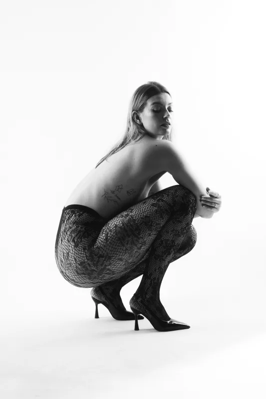 Schwarz-weiß Studioaufnahme einer hockenden Frau mit Netzstrumpfhose und High Heels