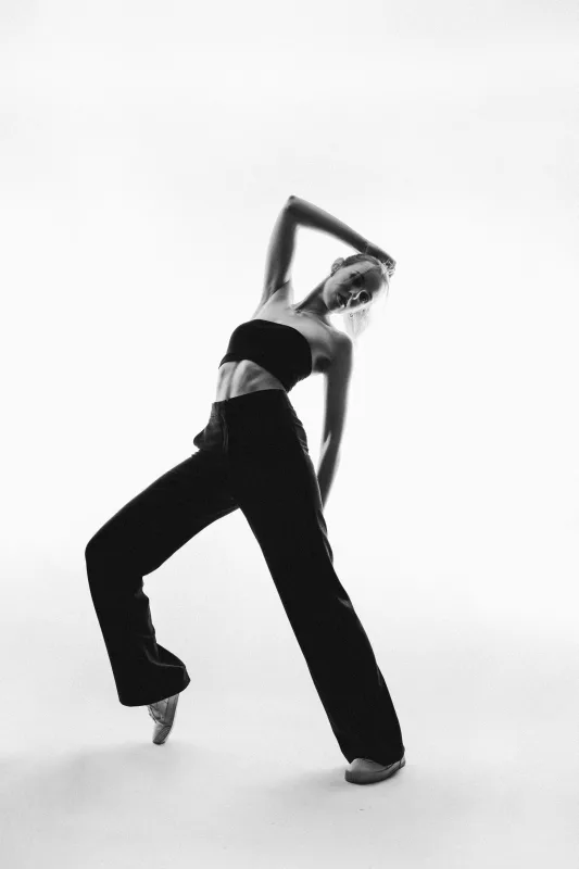 Schwarz-weiß Studiofoto einer Frau in schwarzem Bustier und weiter Hose in dynamischer Pose.