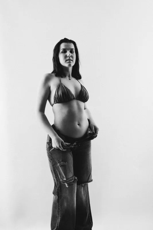 Schwarz-weiß Studioportrait einer Frau in einem Bikini-Top und zerrissener Jeans.
