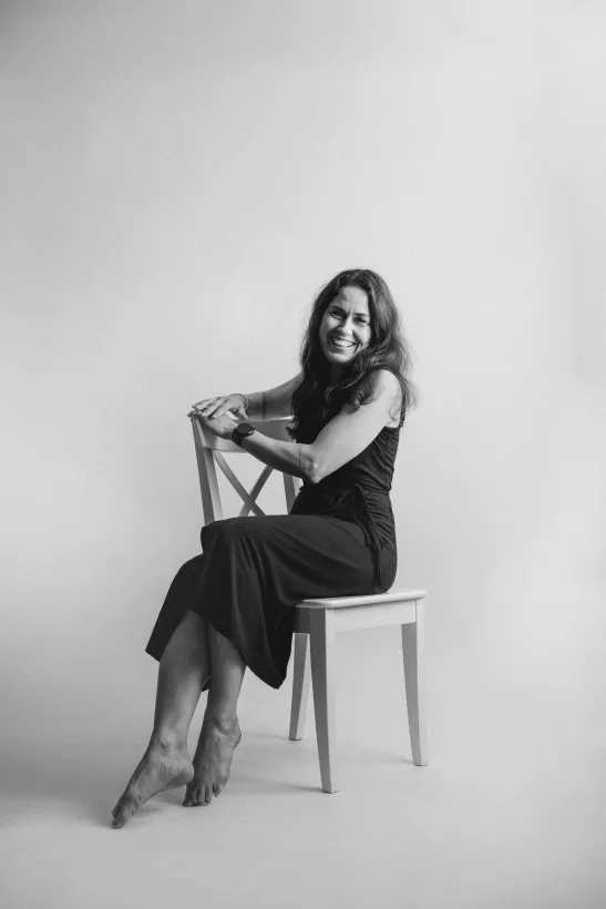 Schwarz-weiß Studioportrait einer lächelnden Frau auf einem weißen Stuhl