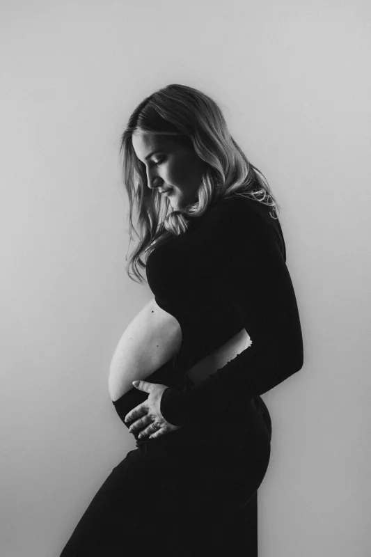 Schwarz-weiß Studioportrait einer schwangeren Frau im Profil.