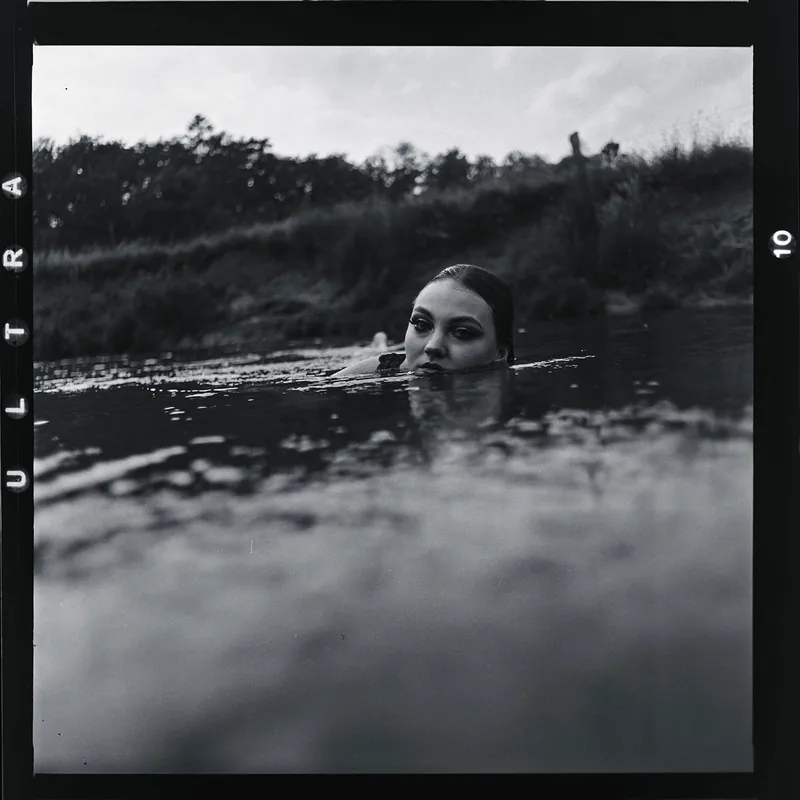 Schwarz-weißes Analogportrait einer Frau, die aus dem Wasser blickt.