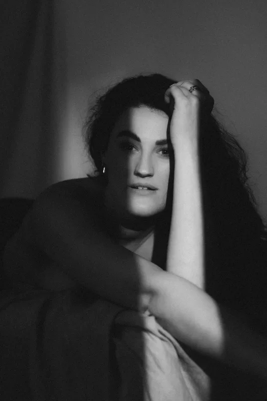 Schwarz-weißes Boudoirportrait einer Frau, die den Kopf auf ihre Hand stützt.