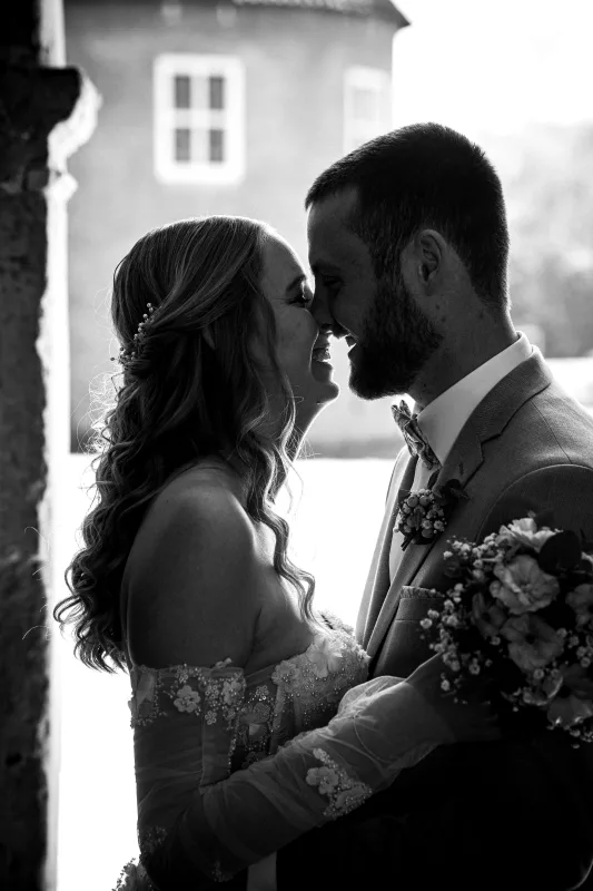 Schwarz-weißes Hochzeitsportrait eines Brautpaares, das sich lächelnd die Stirn berührt.