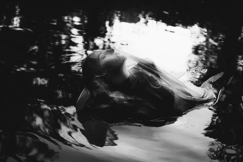 Schwarz-weißes Porträt einer im Wasser treibenden Person mit Blick nach oben.
