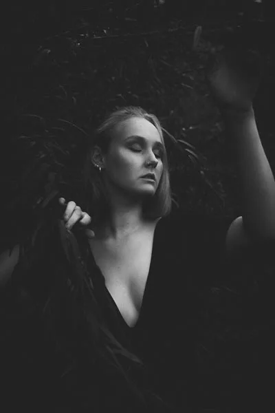 Schwarz-weißes Portrait einer Frau vor dunklem Blattwerk.
