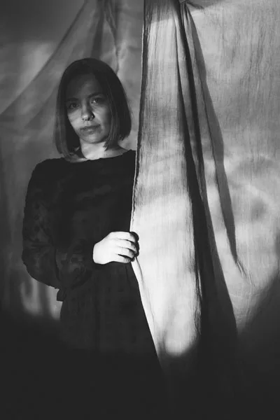 Schwarz-weißes Portrait einer Frau hinter einem hellen, fallenden Stoff.