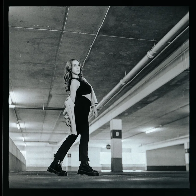 Schwarz-weißes Portrait einer Frau in moderner Kleidung in einem urbanen Parkhaus.