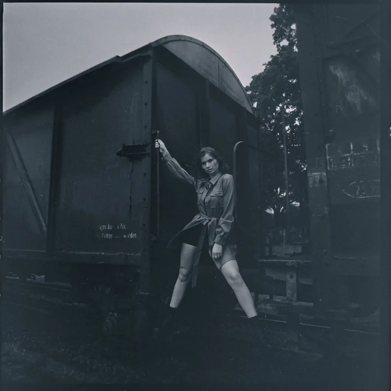 Schwarzweiß-Portrait einer Frau, die an einem alten Eisenbahnwaggon lehnt.