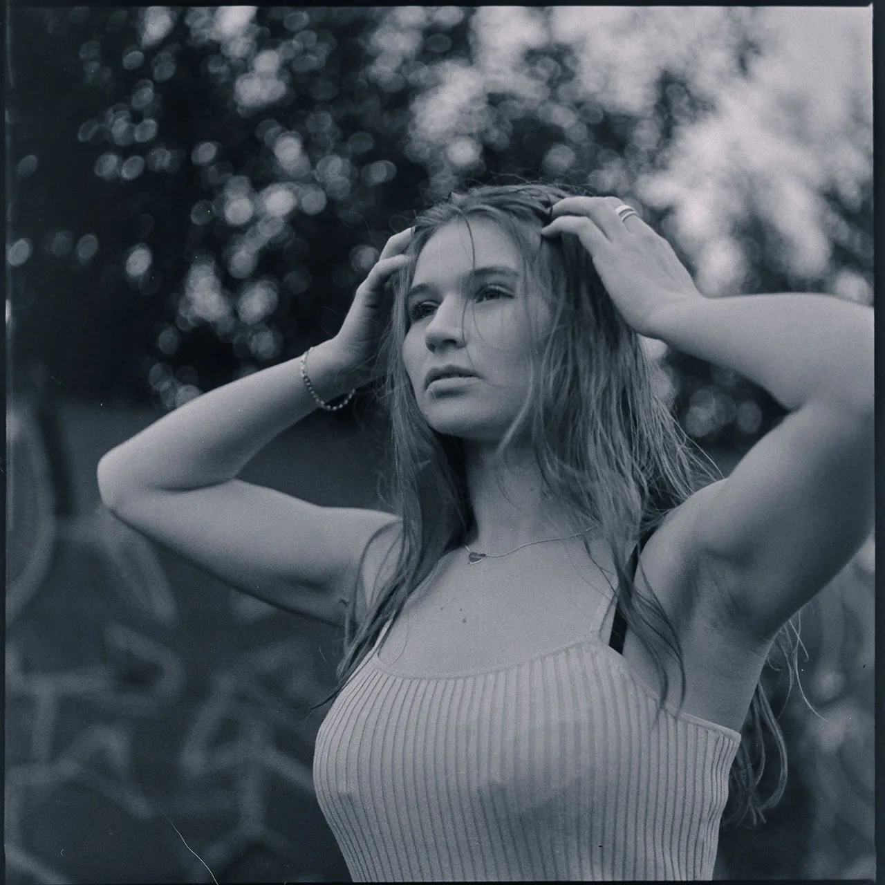 Schwarzweiß-Portrait einer jungen Frau mit den Händen im Haar vor einem unscharfen Hintergrund.