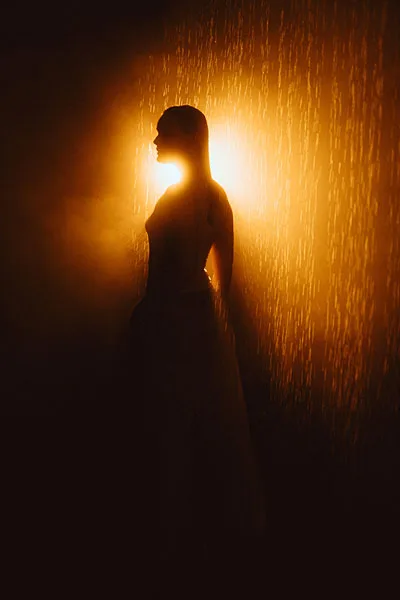 Silhouette einer Frau im Regen bei warmem, goldenem Gegenlicht.