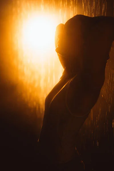 Silhouette einer Person im Regen bei warmem Gegenlicht.