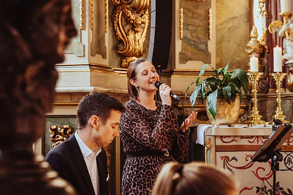 Eine singende Frau bei einem Auftritt in einer prunkvollen barocken Umgebung.