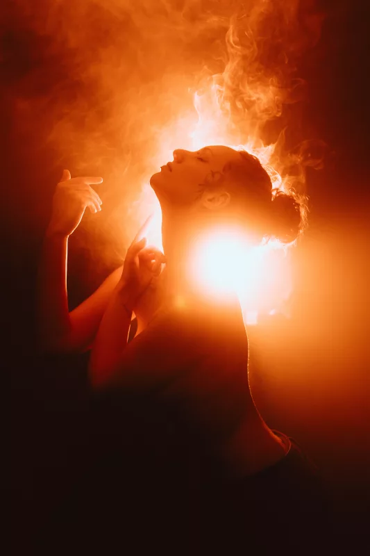 Studioportrait einer Frau im Profil vor leuchtend orangefarbenem Licht und Rauch.