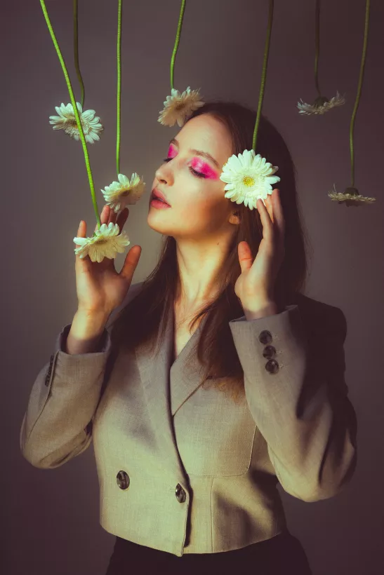 Studioportrait einer Frau mit rosa Augen-Make-up und hängenden weißen Blumen