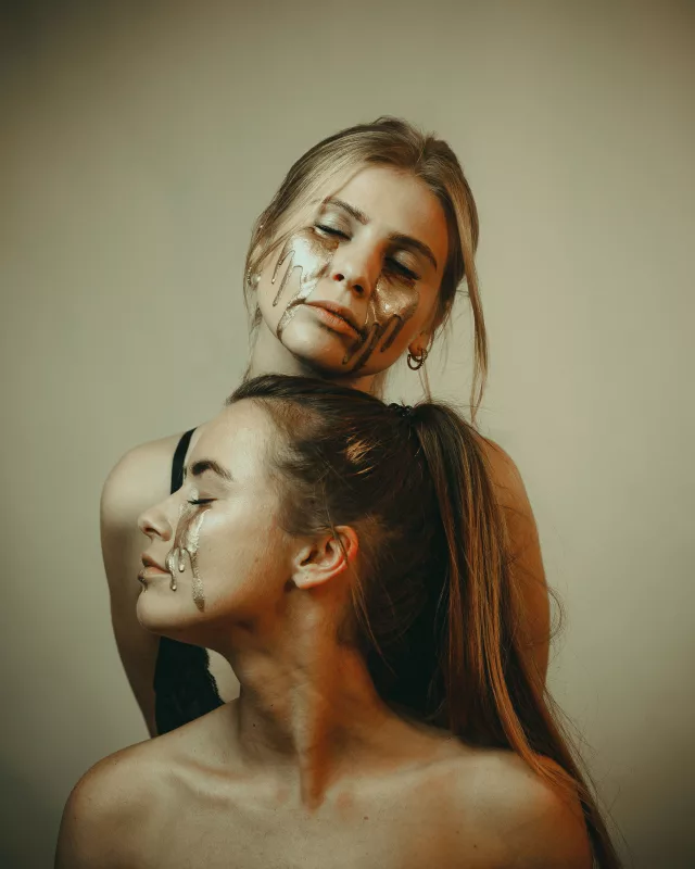 Künstlerisches Studioportrait zweier Frauen mit goldener Flüssigkeit im Gesicht