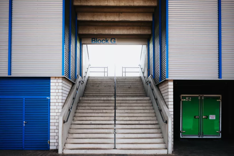 Symmetrische Architekturaufnahme einer Treppe, die zu einem Eingang mit der Aufschrift Block G führt