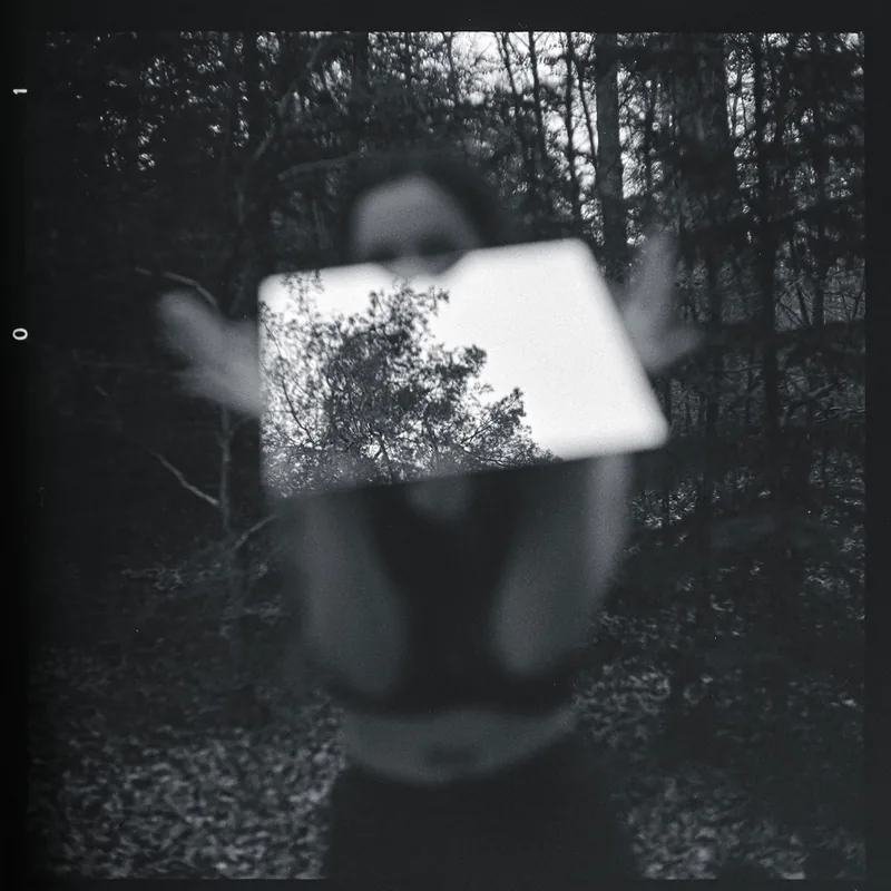 Unscharfes analoges Schwarz-Weiß-Portrait einer Person im Wald mit einem hellen Rechteck voller Baumdetails vor dem Gesicht.