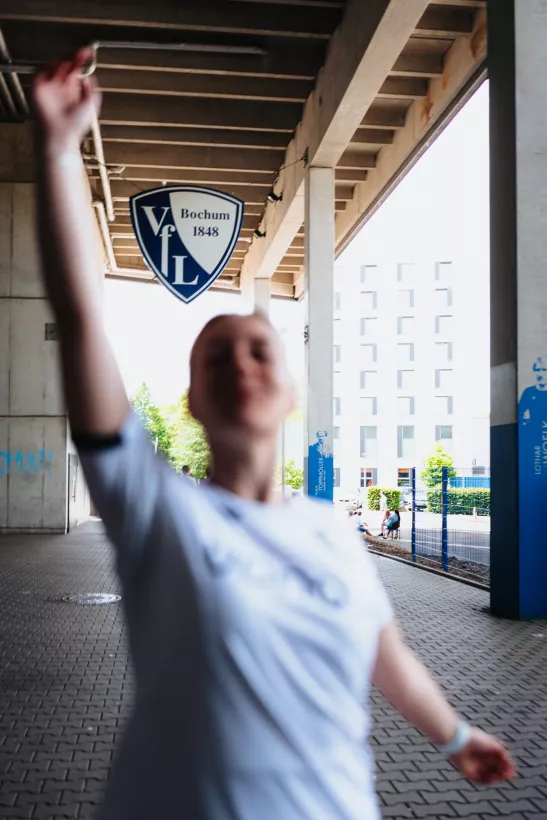 Unscharfes Portrait einer Person mit erhobenem Arm unter einer Betonstruktur