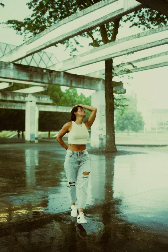 Urbanes Portrait einer Frau in weißem Crop-Top und Jeans unter einer Betonkonstruktion