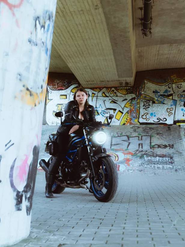 Urbanes Portrait einer Frau auf einem schwarzen Motorrad vor einer Graffiti-Wand