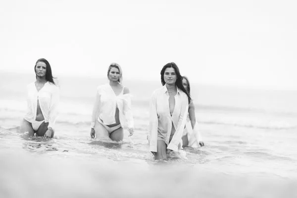 Vier Frauen in weißen Oberteilen stehen im seichten Meerwasser.