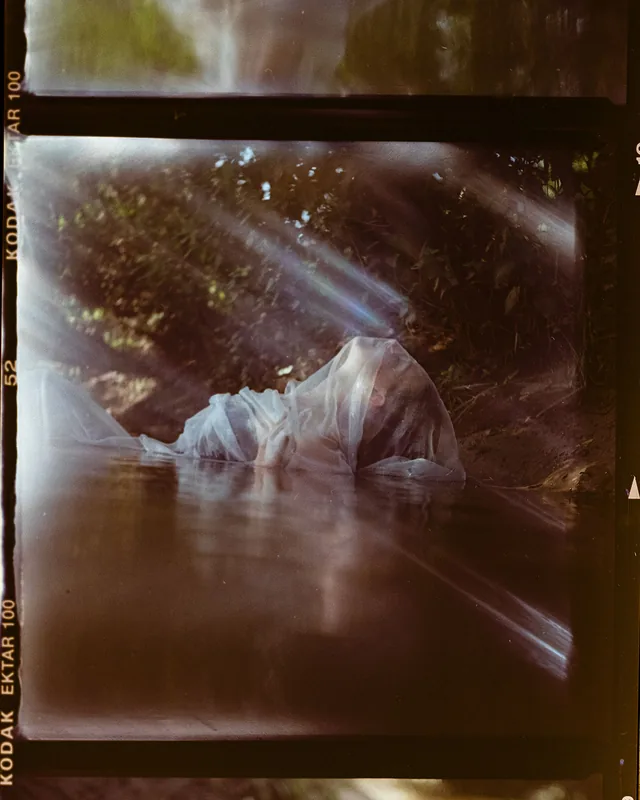 Eine mit weißem, transparentem Stoff bedeckte Person im Wasser, analoges Portrait.