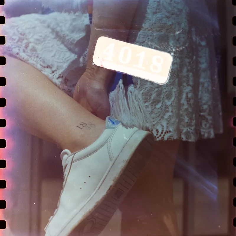Detailaufnahme eines Beins mit weißem Sneaker, hellem Spitzenrock und einem kleinen Tattoo am Knöchel