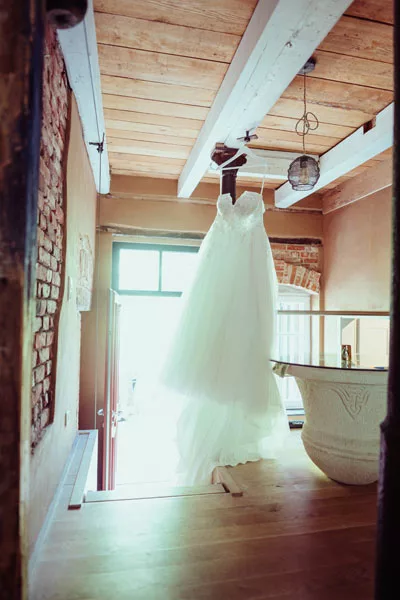 Weißes Hochzeitskleid, das an einem Holzbalken in einem rustikalen Raum hängt