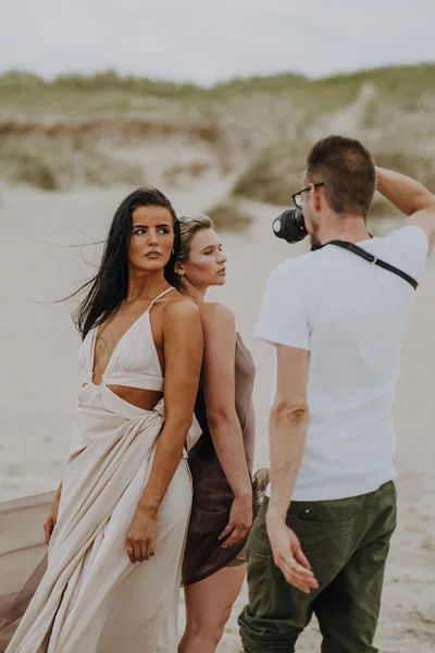 Zwei Frauen in eleganten Kleidern bei einem Fotoshooting in einer Dünenlandschaft.
