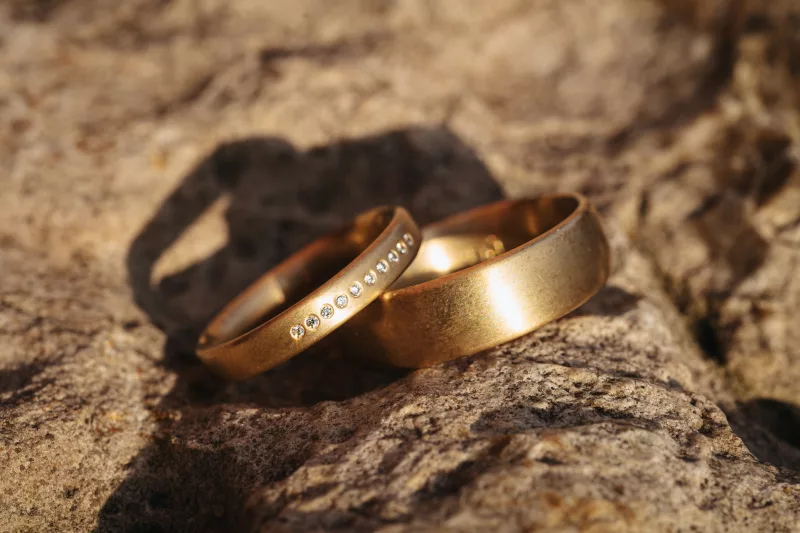 Zwei goldene Eheringe mit kleinen Steinen auf einer rauen Gesteinsoberfläche.