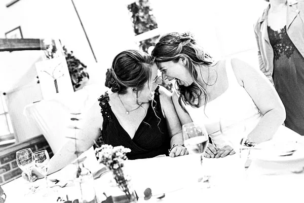 Zwei lachende Frauen an einem festlich gedeckten Hochzeitstisch in Schwarz-Weiß.